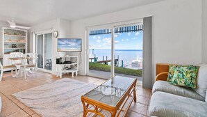 A spacious living room with a large glass table, a sofa, and a TV. There is a balcony with a view of the sea. - Windsurfers Paradise, Unit 120 (South Padre Island)