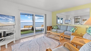 A living room with a large sliding glass door leading to a balcony with a view of the ocean. - Windsurfers Paradise, Unit 120 (South Padre Island)