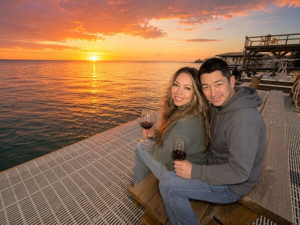 A couple sitting on a wooden bench overlooking a body of water at sunset.