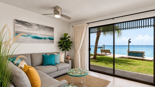 A living room with a sofa, a coffee table, a painting, and a view of the beach through large glass doors. - Windsurfers Paradise, Unit 121 (South Padre Island)