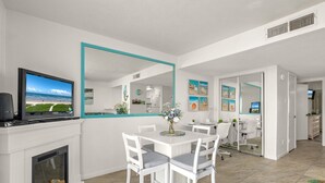 A modern dining area with a white table and chairs, a fireplace, and a large mirror above the table. - Windsurfers Paradise, Unit 121 (South Padre Island)