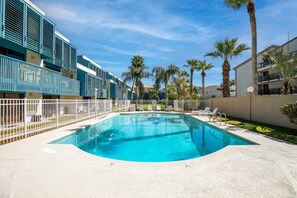 A swimming pool surrounded by a white fence, with palm trees and a clear blue sky in the background.