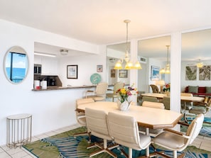 A modern dining area with a round table, chairs, a vase of flowers, and a view of the ocean through a window.