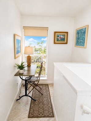 A room with a dining table, chairs, a lamp, a potted plant, a patterned rug, and framed pictures on the walls.