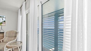 A balcony with white shutters, a wicker chair, and a small table. - Luxury Bayfront Dream Condo (South Padre Island)