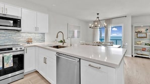 A modern kitchen with white cabinetry, stainless steel appliances, and a large island with a sink. - Luxury Bayfront Dream Condo (South Padre Island)