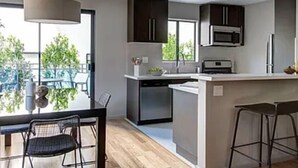 A modern kitchen with a central island, dark cabinets, and a view of greenery outside. - Westwood Living - Gorgeous Modern One Bedroom Available For Rent, Close to UCLA (Los Angeles)