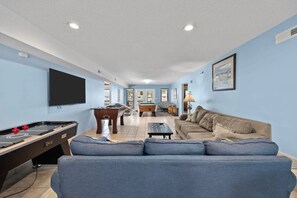 A living room with a pool table, a sofa, and a television.