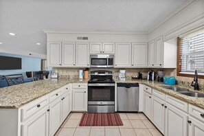 A modern kitchen with white cabinets, granite countertops, stainless steel appliances, and a built-in microwave.
