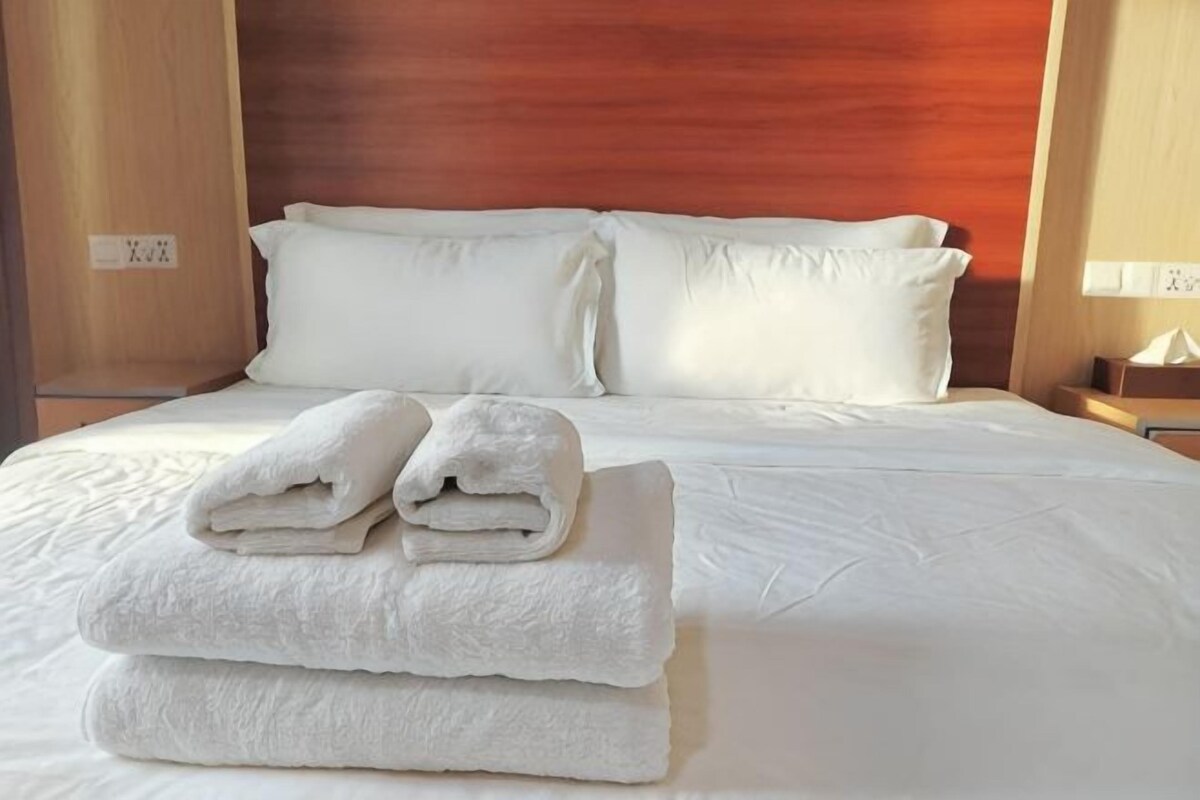Un lit bien fait, avec du linge de lit et des serviettes blanches, une tête de lit en bois et une table de chevet avec une lampe.