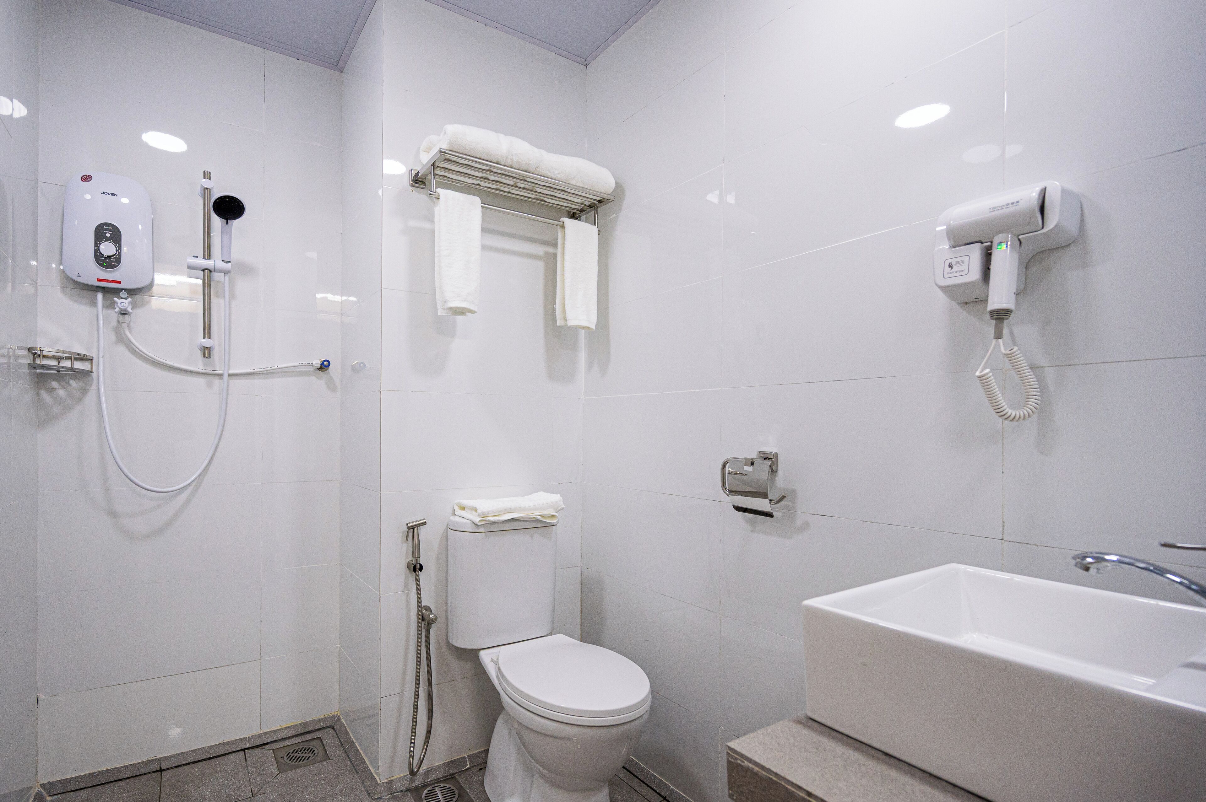 A modern bathroom with a toilet, a shower with a handheld showerhead, a hairdryer, and a sink.