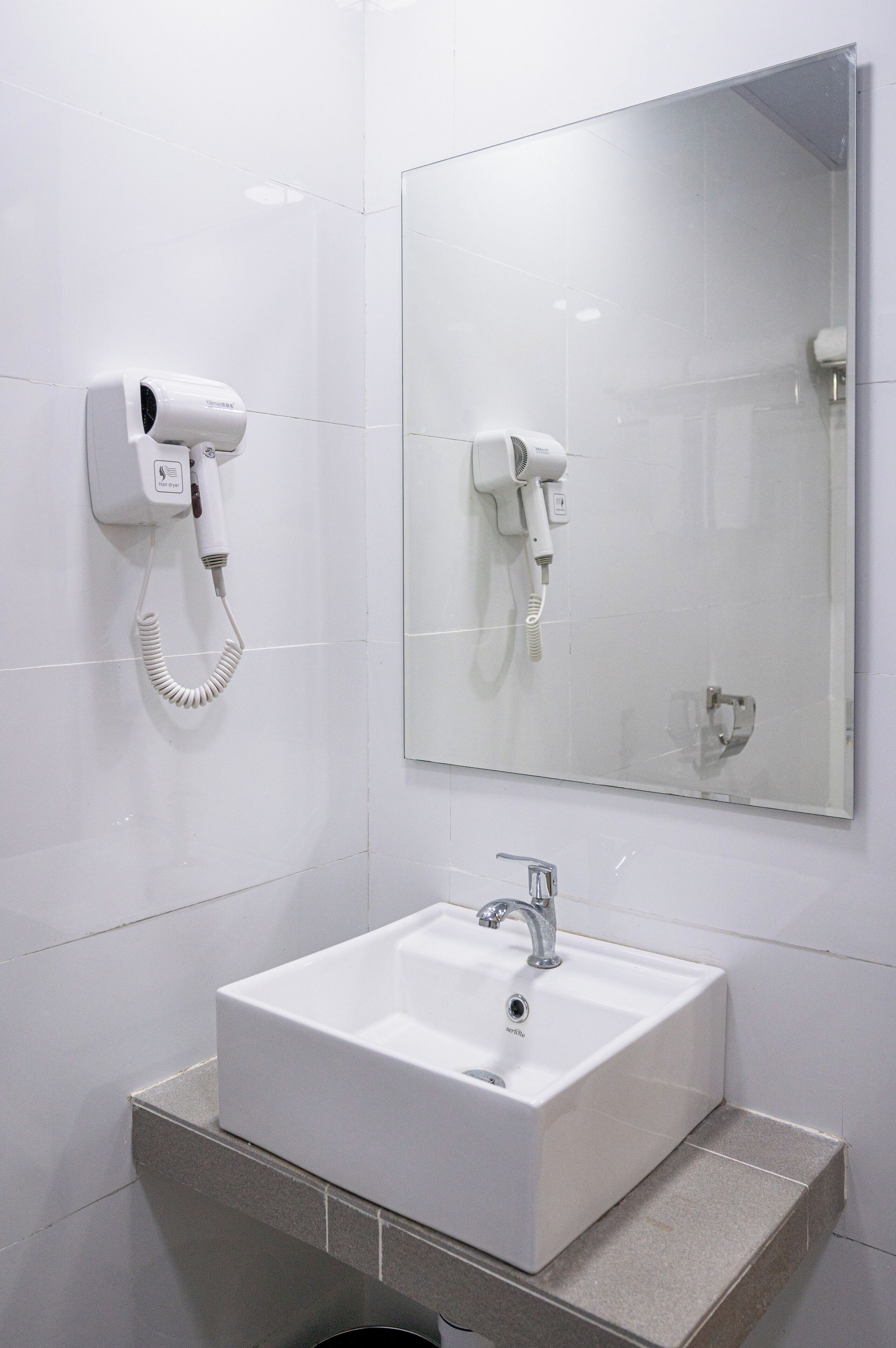 Un baño con un lavamanos blanco, un espejo y un secador de pelo montado en la pared.