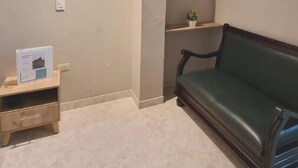 Una stanza con un divano verde scuro, un tavolino in legno con una scatola, una mensola a parete con una pianta e una luce a incasso nel soffitto.
