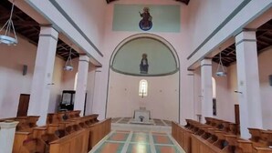 Interno di una chiesa con panche in legno, pavimento piastrellato e alto soffitto in legno.