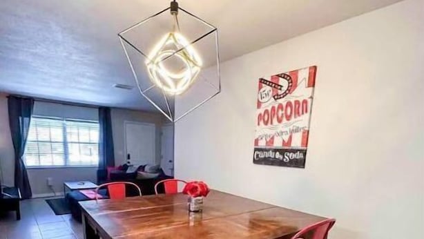 A dining area with a wooden table and red chairs, a hanging light fixture, and a wall poster. - 5 Rooms • Great Location • Red Haven Retreat (Tampa)