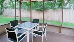 A covered patio area with a table and chairs, large windows, and a view of a backyard with a wooden fence. - 5 Rooms • Great Location • Red Haven Retreat (Tampa)