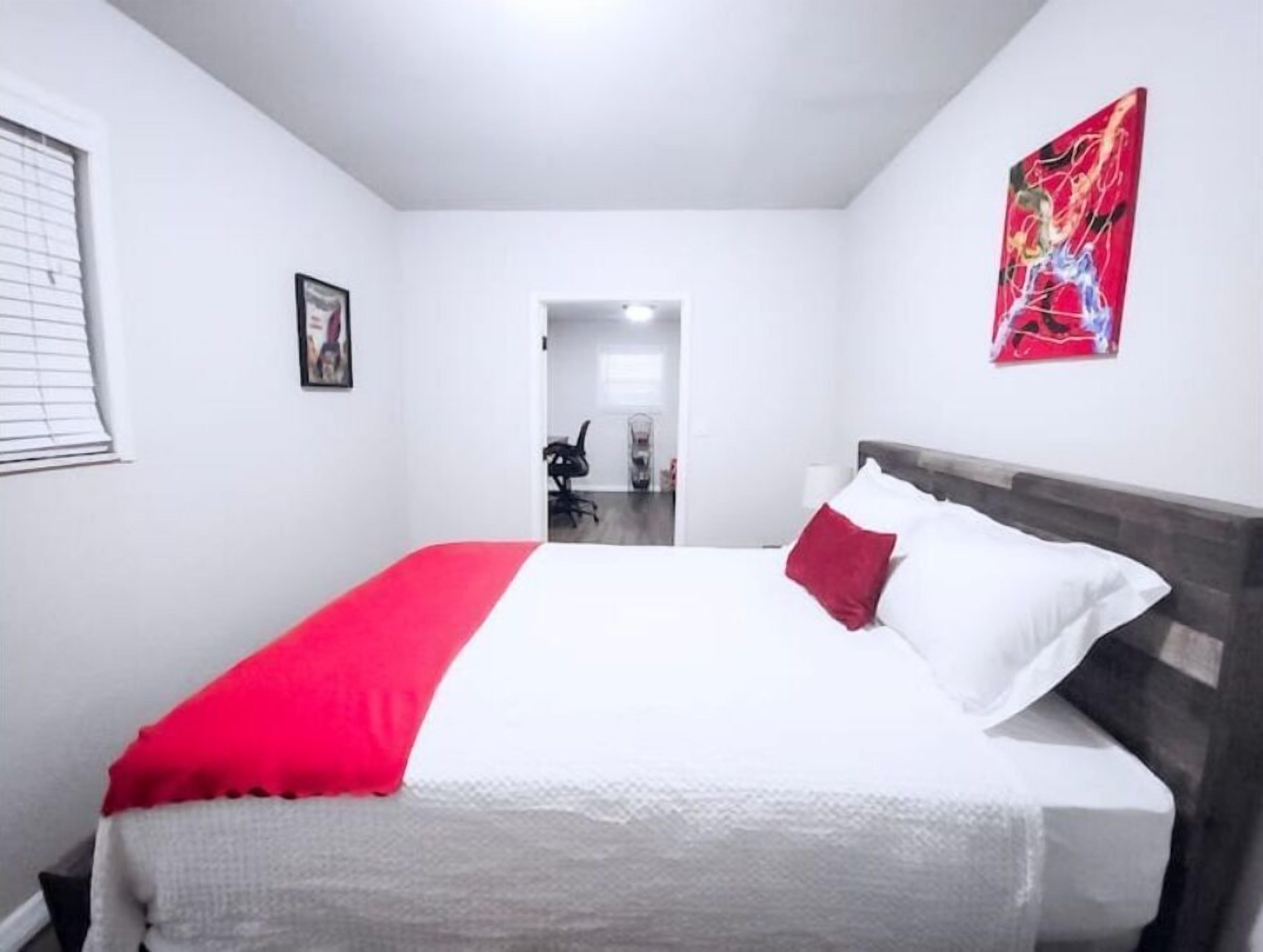 Habitación de hotel con cama, colcha roja y blanca, almohada roja, almohada blanca, un cuadro en la pared y un cuadro abstracto rojo.