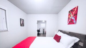 A hotel room with a bed, a red and white bedspread, a red pillow, a white pillow, a framed picture on the wall, and a red abstract painting. - 5 Rooms • Great Location • Red Haven Retreat (Tampa)
