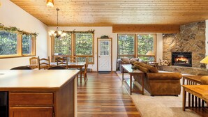 Un interior de madera con cocina, comedor y sala de estar, destacando una chimenea y ventanas amplias.