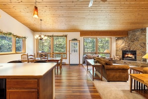 Un interior de madera con cocina, comedor y sala de estar, destacando una chimenea y ventanas amplias.