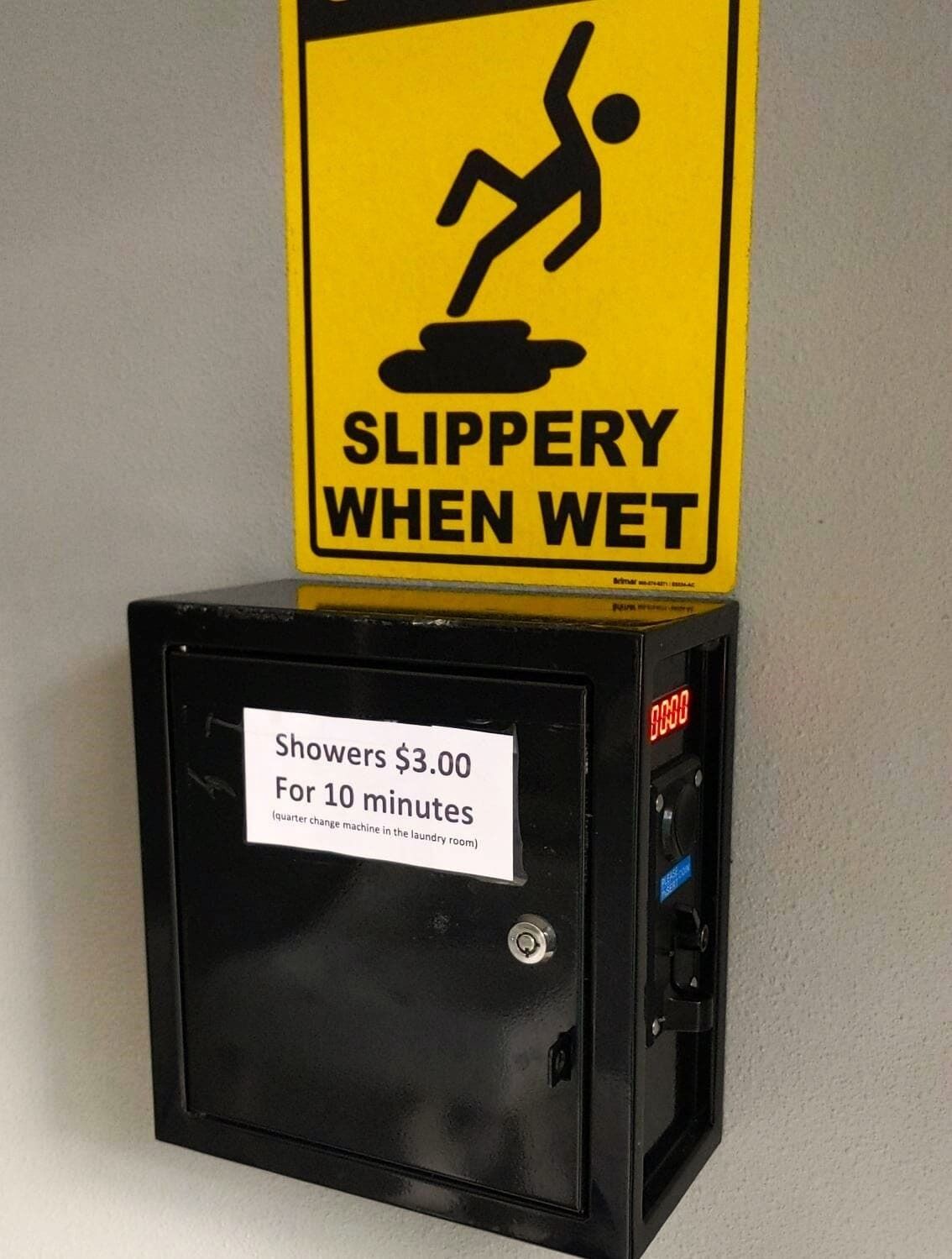 Schild mit Warnung vor Rutschgefahr bei Nässe und eine Münz-Dusche mit Preisschild.