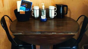 Ein runder Holztisch mit vier schwarzen Stühlen, einer schwarzen Kaffeekanne, zwei weißen Tassen, einer schwarzen Tasse, einer schwarzen Ablage und einem schwarzen Korb mit einer Broschüre.