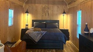 Ein Schlafzimmer in einer Holzhütte mit einem Bett, zwei Nachttischlampen, einem Deckenventilator und rustikaler Einrichtung.