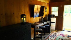 Eine kompakte Küche mit Holzwänden, einem Flachbildfernseher, einem Kühlschrank und einem kleinen Tisch mit zwei Hocker.