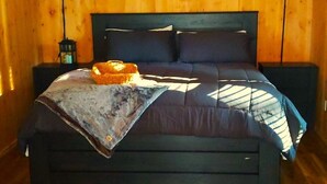 Een slaapkamer in een houten chalet, met een bed, twee nachtkastjes en een hanglamp.
