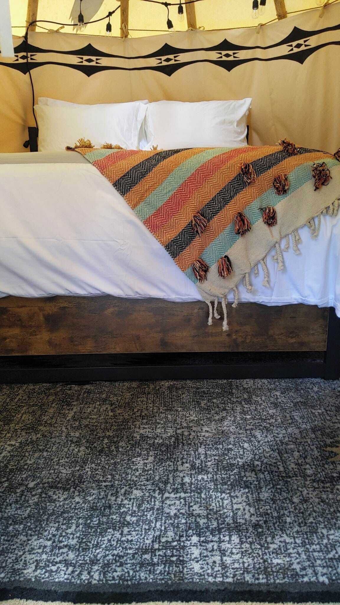 Una cama con una manta estampada, almohadas blancas y un cabecero de madera oscura.