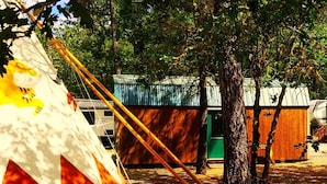 En campingplads med et stort telt, en mindre træbygning og et træ.