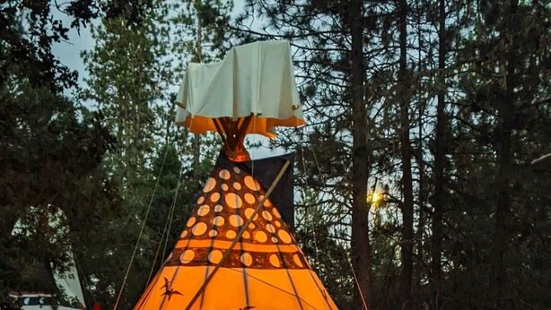 A conical tent with a patterned design, set up in a forested area. - Sky Spirit -Luxury Glamping 18' Tipi -  Restrooms and Showers are only a short walk away. (O'Brien)