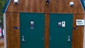A wooden building with two green doors, each marked with a restroom sign. - Sky Spirit -Luxury Glamping 18' Tipi -  Restrooms and Showers are only a short walk away. (O'Brien)