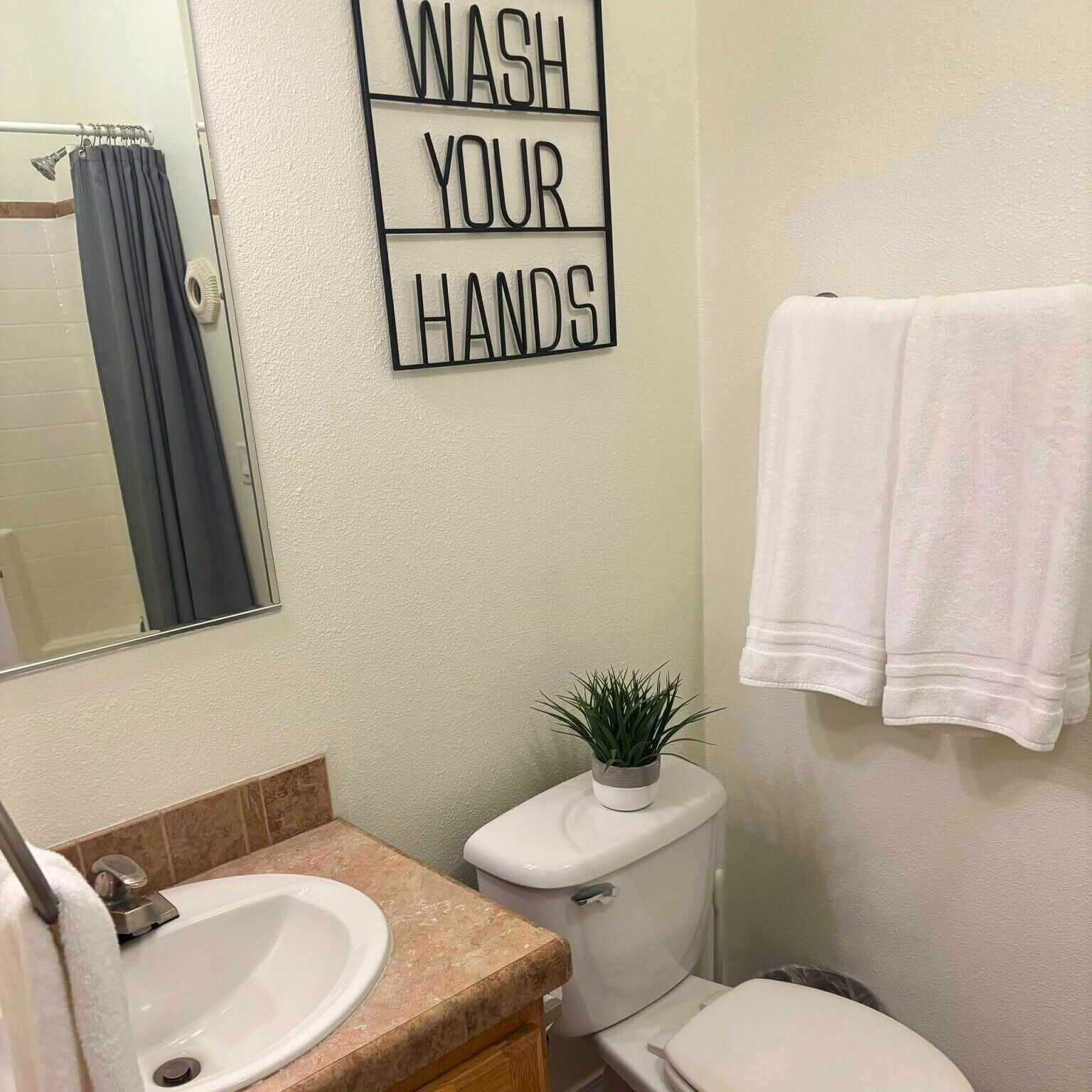 Une salle de bain équipée d’un lavabo, de toilettes et d’une pancarte fixée au mur sur laquelle on peut lire : « LAVEZ-VOUS LES MAINS ».