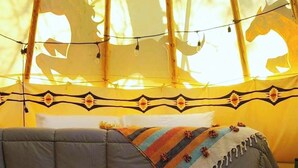 A bed with a patterned blanket, a canopy with horse silhouettes, and a string of lights. - Wild Horses Luxury Tipi -  Restrooms and Showers are only a short walk away. (O'Brien)