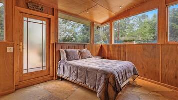 A wooden bedroom with a bed, large windows, and a stone floor.
