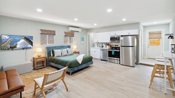 Une chambre moderne et bien éclairée, comprenant un lit, un petit coin salon, une kitchenette et une table à manger.