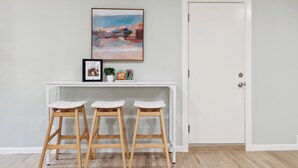 Une pièce comprenant une console blanche, trois tabourets en bois, un tableau encadré et une porte.