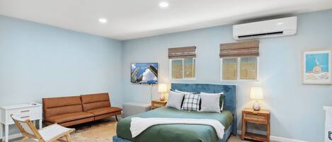 A bedroom with a bed, a sofa, a desk, and an air conditioning unit.