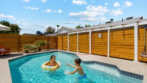 Une piscine avec une terrasse en bois, une clôture en bois et un ciel d’un bleu limpide.
