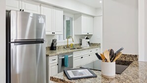 A modern kitchen with white cabinets, a stainless steel refrigerator, a granite countertop, and a coffee maker. - Family Friendly Retreat | Pool & Putting Green (Tempe)