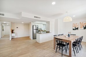 Een moderne keuken met witte kasten en roestvrijstalen apparatuur, een eethoek met een houten tafel en stoelen, en een hal met houten vloeren.