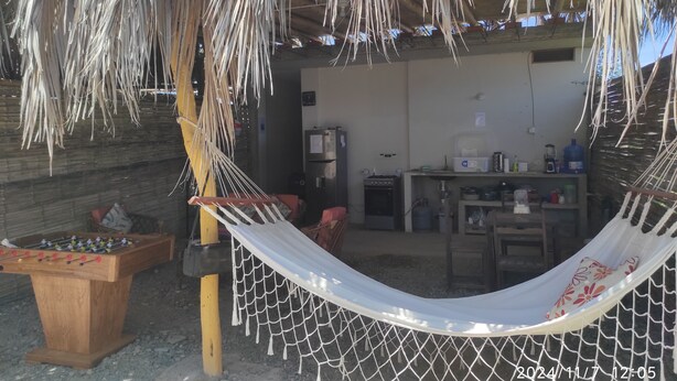 A hammock under a thatched roof, a wooden foosball table, and a kitchen area with a refrigerator and water dispenser.
