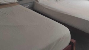 A room with two single beds, a bedside table with a lamp, and a window with a curtain.