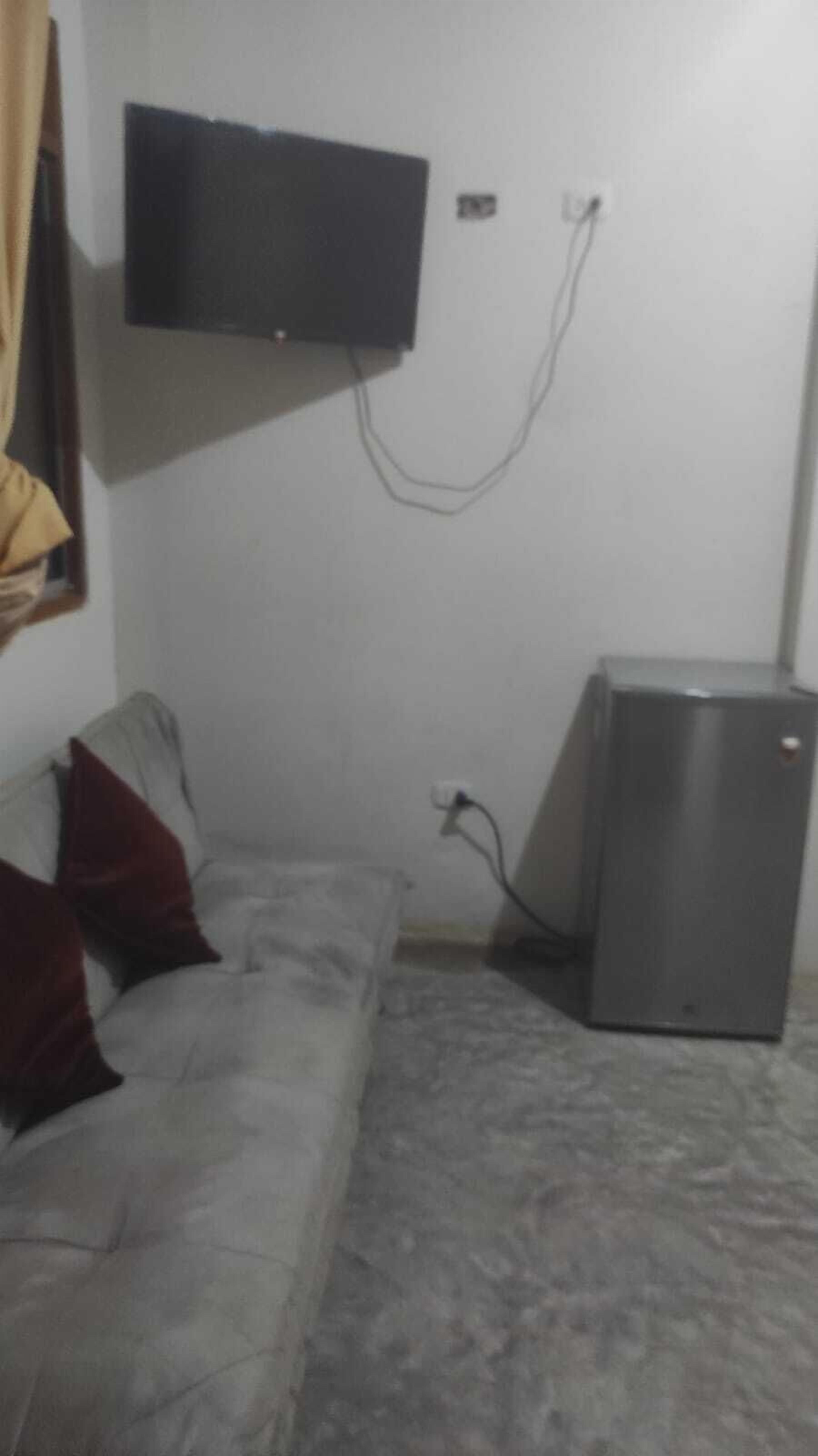 A room with a white sofa, a flat-screen TV mounted on the wall, and a small refrigerator.
