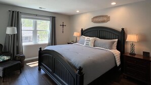 A bedroom with a large bed, two bedside tables with lamps, a cross on the wall, and a window with curtains. - "Relaxing Retreat"  7 Night Discount~No Stairs~Indoor Pool~Golf~Trout~Pickleball (Branson)