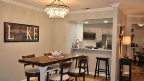A dining area with a wooden table, four chairs, a chandelier, and a kitchen in the background. - "Relaxing Retreat"  7 Night Discount~No Stairs~Indoor Pool~Golf~Trout~Pickleball (Branson)