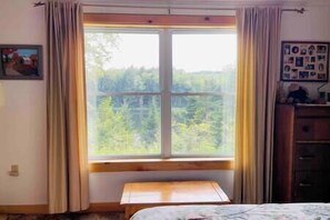 A bedroom with a large window, a bed, a small table, and a dresser. - Clear Pond Cottage a Retreat on Private Pond (Hyde Park)
