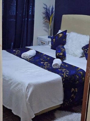 A neatly made bed with a blue and gold patterned bedspread, white pillows, and a white throw blanket.