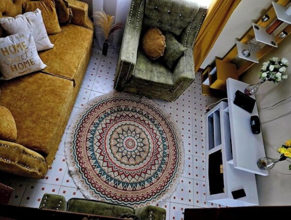 A cozy living room with a patterned rug, a sofa, a chair, and a small table with a vase of flowers.
